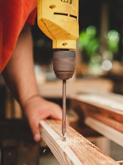 Close-up of a worker drilling a hole into a wooden beam during construction.