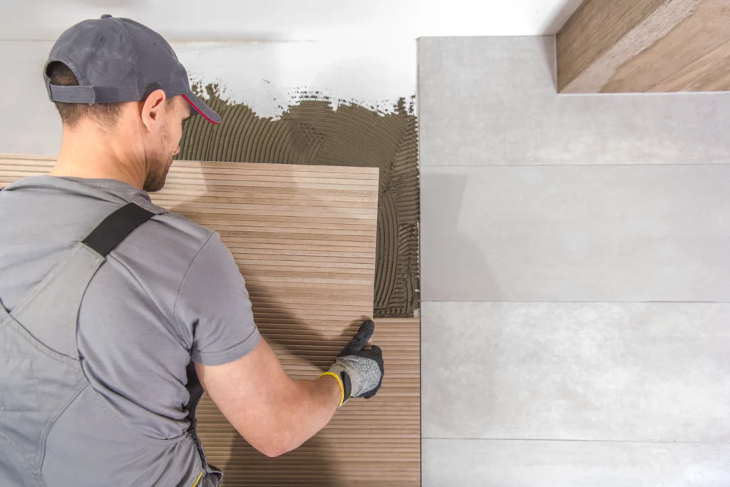 Construction worker installing large-format tiles on the floor using adhesive mortar.