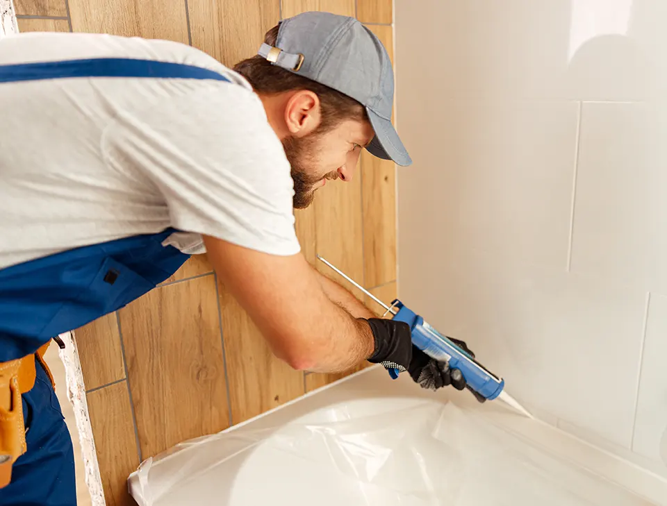 Worker applying caulk in a bathroom corner to seal the space.