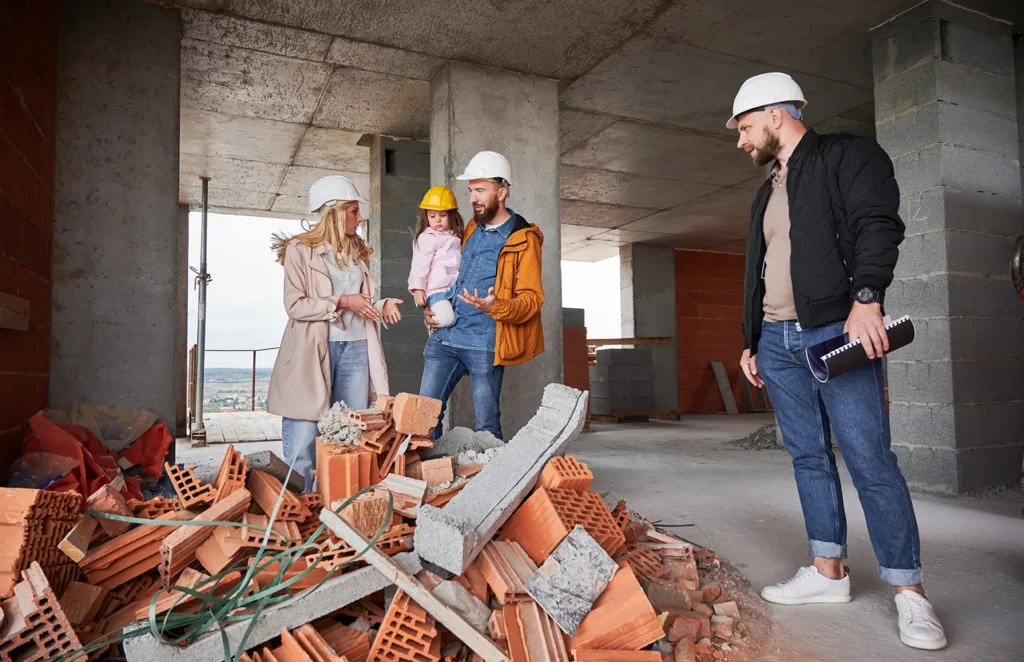 Family and construction team on a building site discussing renovation plans, surrounded by building materials.