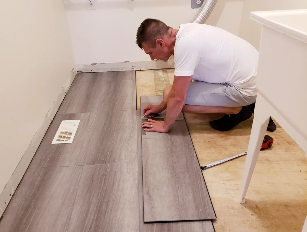 Man carefully installing vinyl flooring panels in a home renovation project.