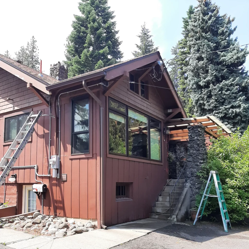 Exterior of a rustic home undergoing renovation, with ladders and equipment in place, highlighting Coca Construction's restoration work.