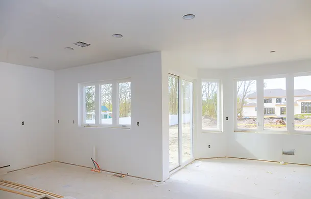 An unfinished room with freshly installed drywall and windows, ready for interior finishing.