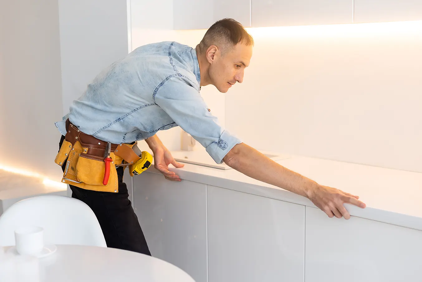 Skilled worker carefully measuring and aligning a cabinet during trim and crown molding installation in a modern kitchen.