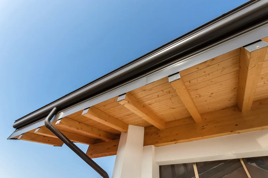 Close-up of a house's roof eaves with wood detailing and new gutter installation under a clear blue sky.