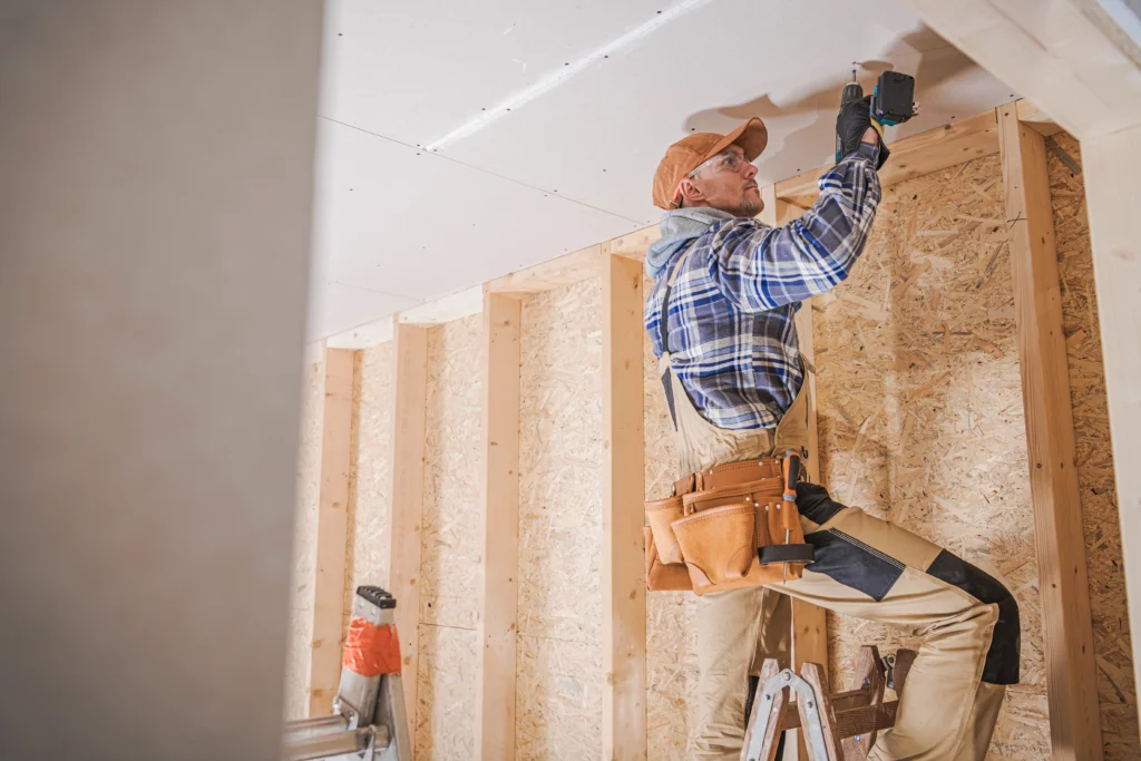 Worker installing drywall on the ceiling of a framed room.