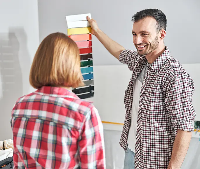 Smiling man holding a color palette, discussing paint choices with a woman.