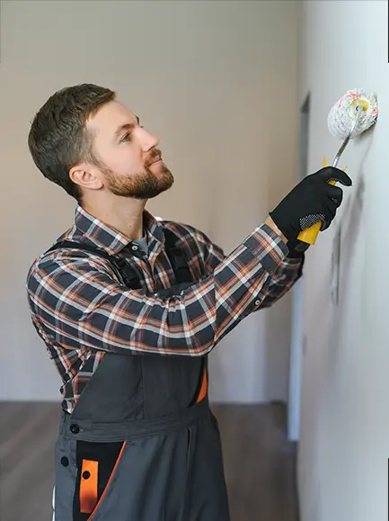 Male painter applying a fresh coat of paint to an interior wall using a roller.