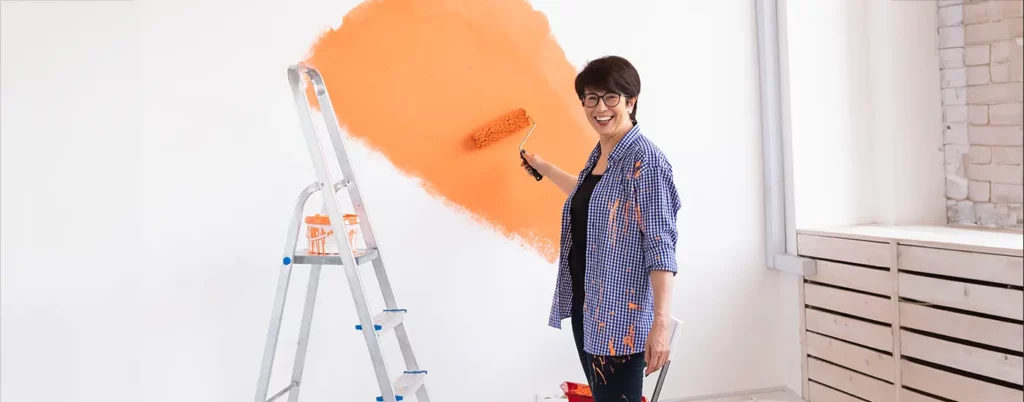 Smiling woman painting a wall orange with a roller brush.