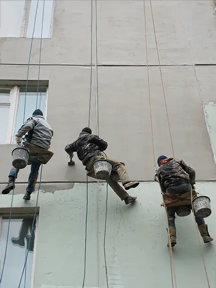 Three workers painting the exterior of a tall building while suspended from ropes.