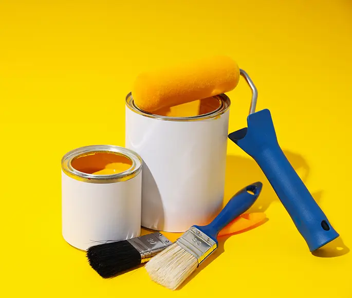 Paint cans, roller, and brushes on a bright yellow background, essential tools for house painting.