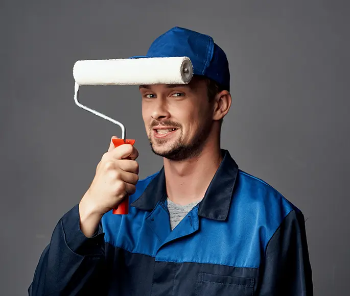 Smiling professional painter in blue uniform holding a paint roller, ready for a house painting job.