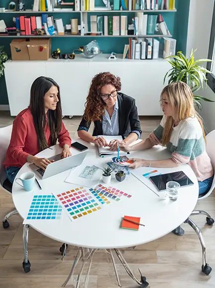 Three women planning a project with color swatches at a table in an office.